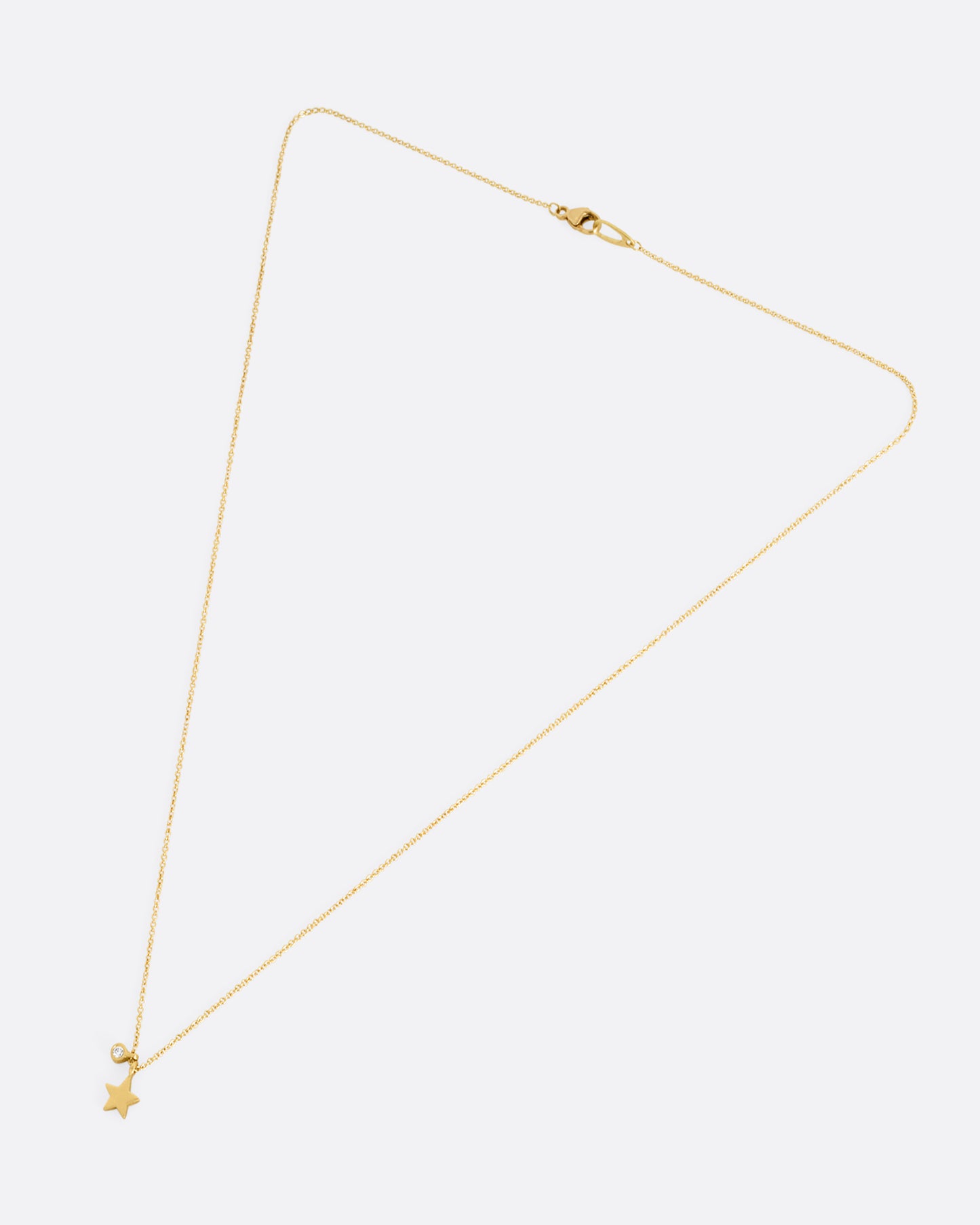 A yellow gold cable chain necklace with a tiny diamond tag and star charm. Shown closed lying flat from the front.