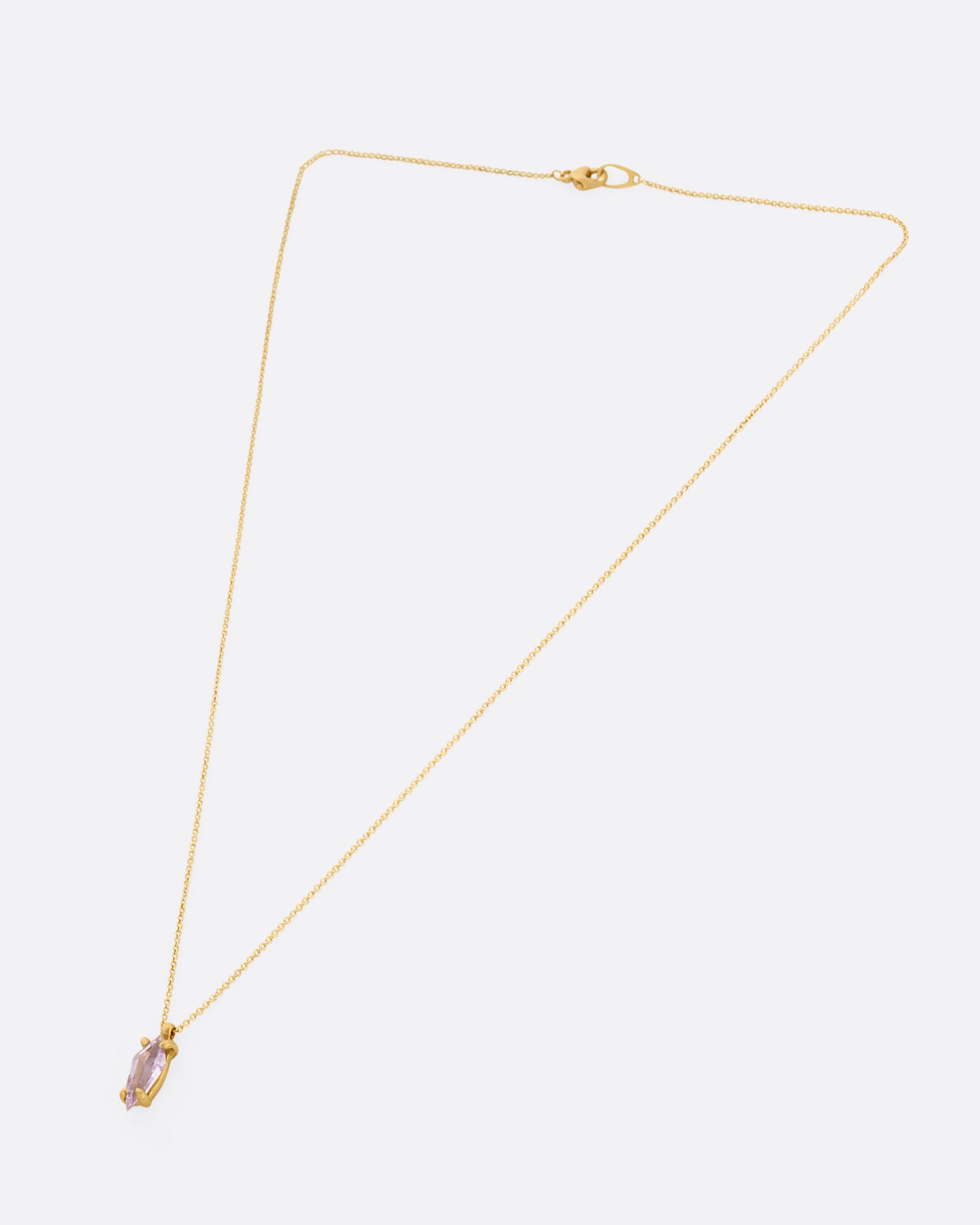 A yellow gold cable chain necklace with a single pink sapphire pendant. Shown closed lying flat from the front.
