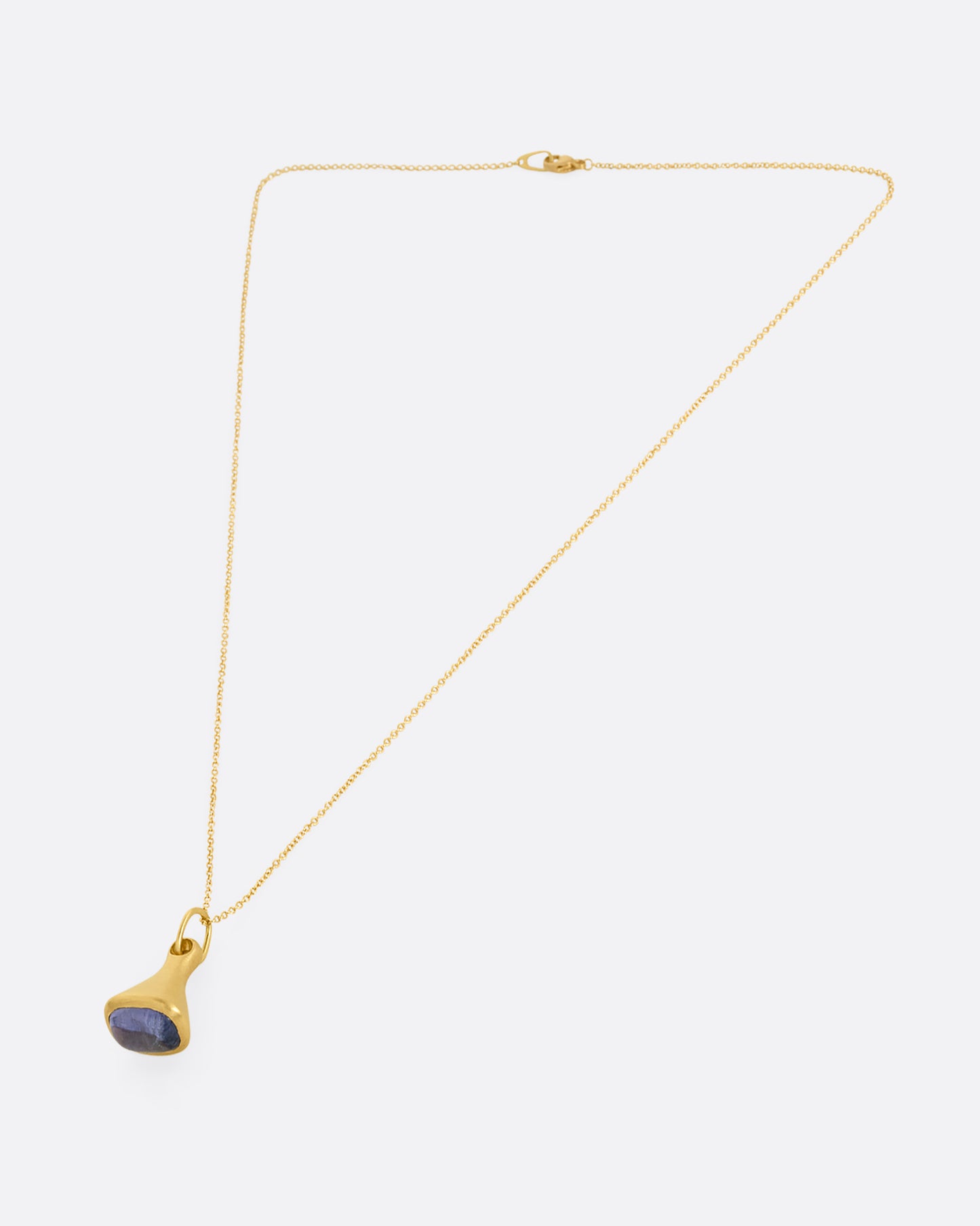 A yellow gold cable chain necklace with a bell shaped pendant with a tanzanite cabochon at the base. Shown closed lying flat at an angle from the front.