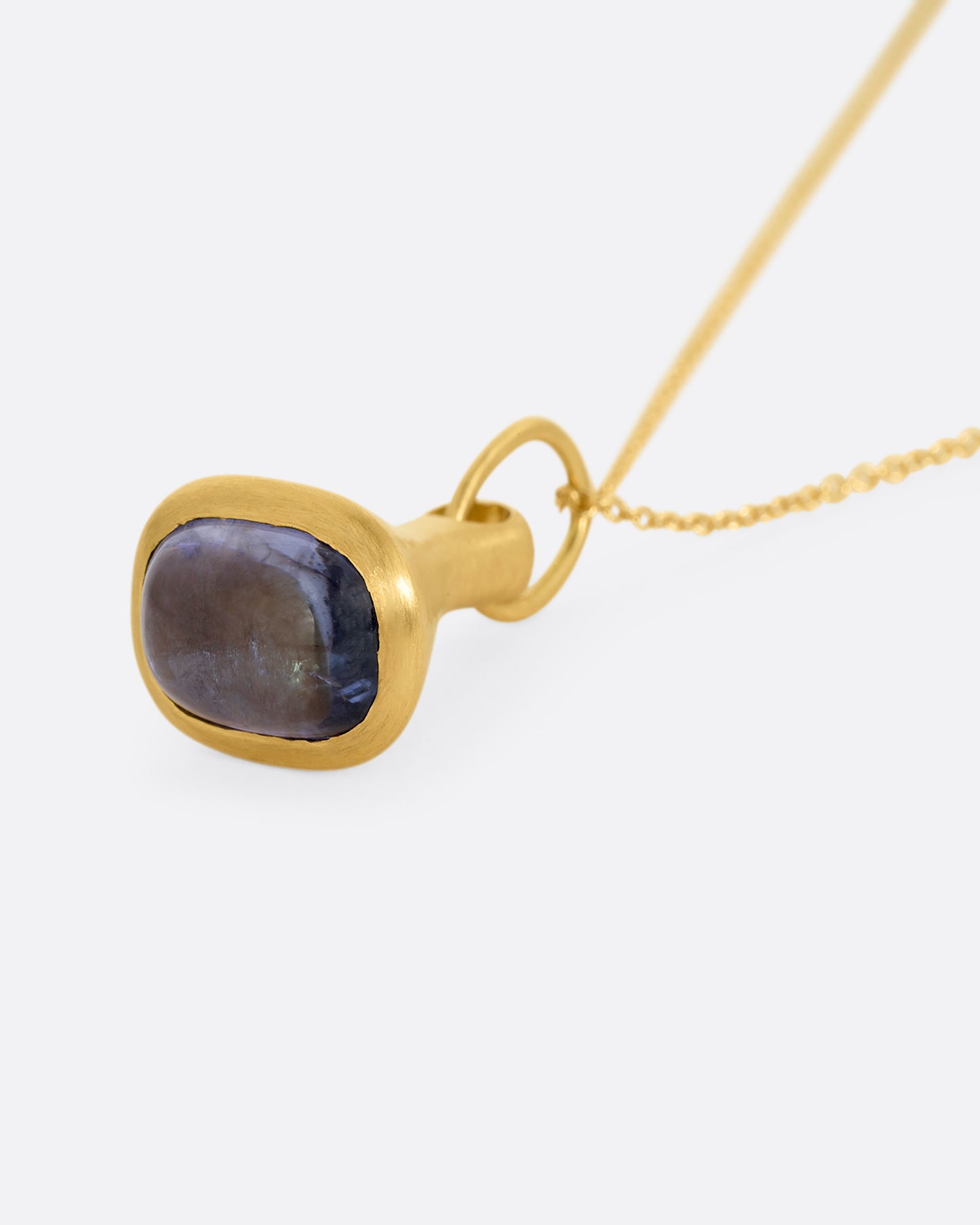 A yellow gold cable chain necklace with a bell shaped pendant with a tanzanite cabochon at the base. Shown lying flat from the bottom.
