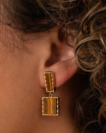 Vintage drop earring in 18k yellow gold worn on an ear, a rectangular tiger's eye stud with a square tiger's eye drop in rope-edged gold frames