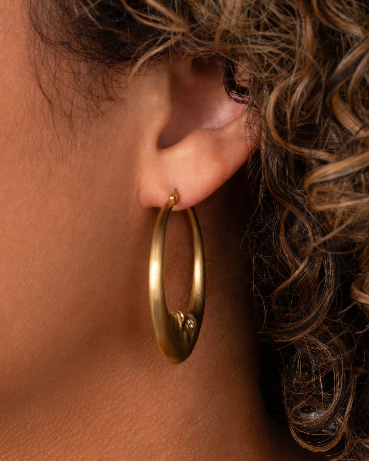 yellow gold crescent shaped oop earring with diamond eyes shown worn in an ear