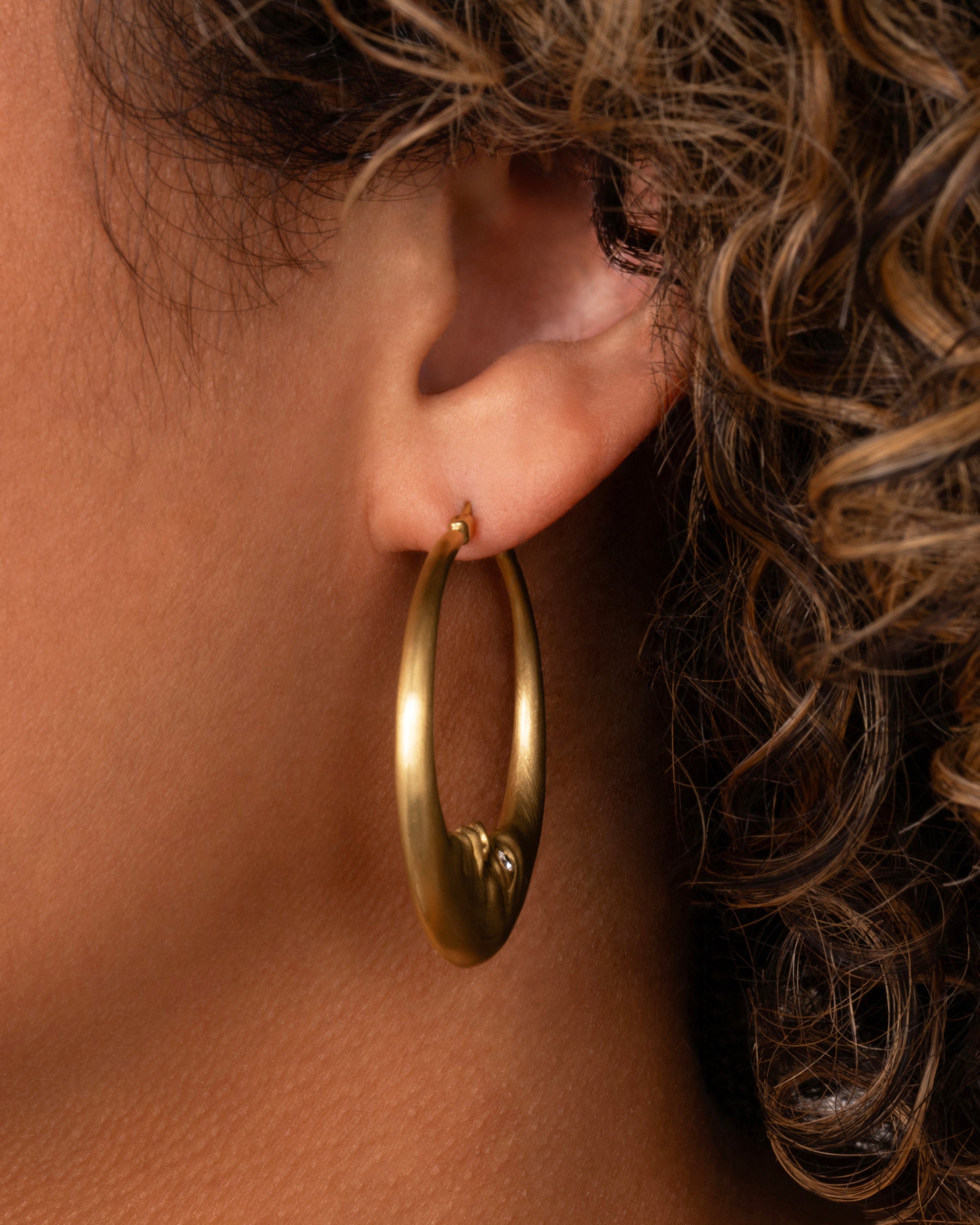yellow gold crescent shaped oop earring with diamond eyes shown worn in an ear