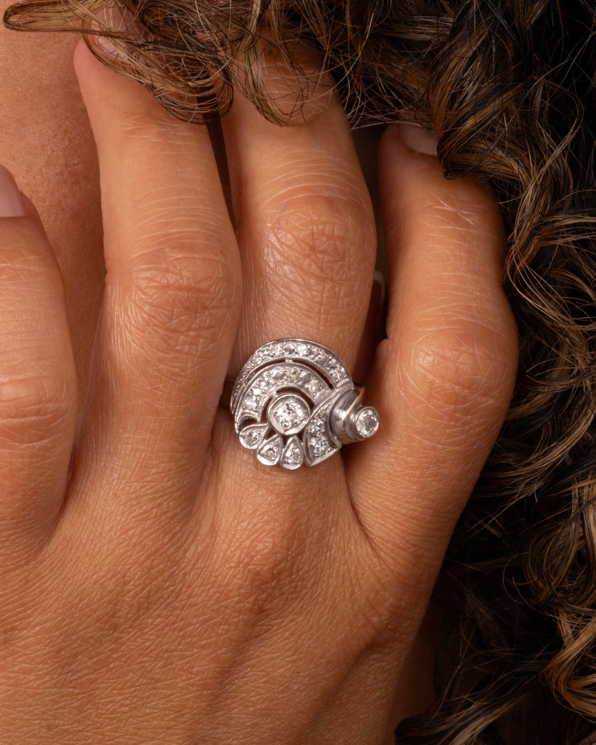 A white gold curving ring with diamonds. Shown worn on a finger.