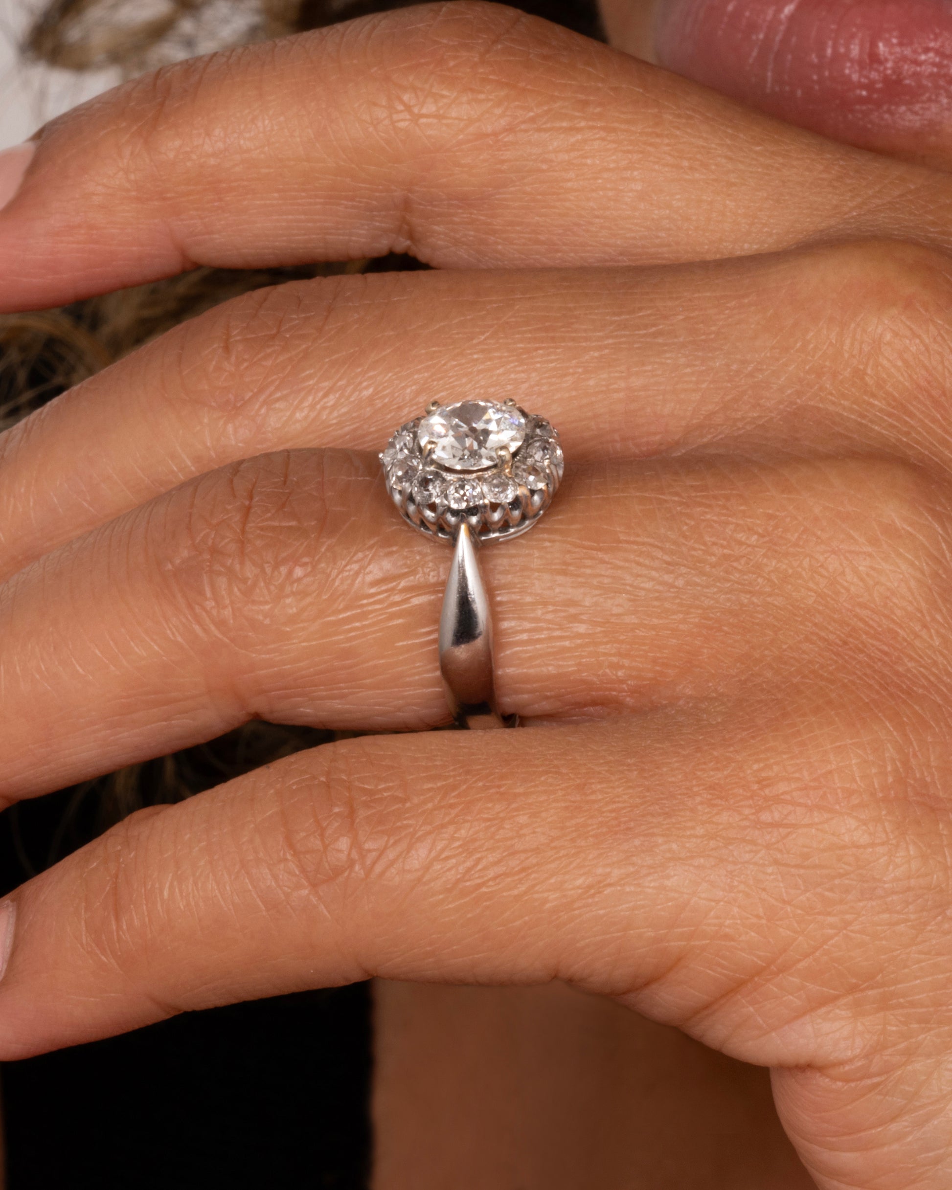 A white gold ring with a tapered band and a flower-shaped cluster of diamonds, shown worn on a hand.