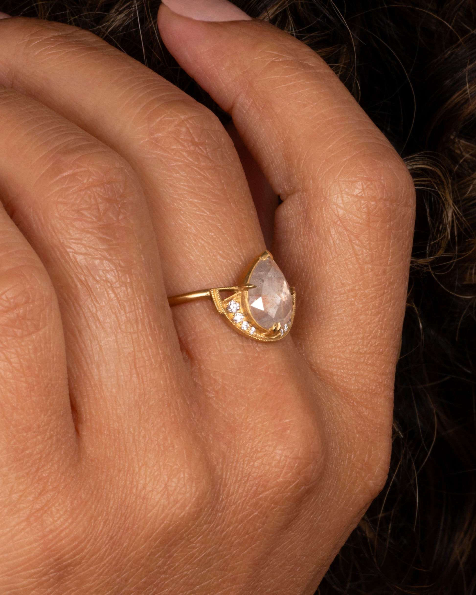 A rose cut, icy gray diamond sits at the center of this ring with a half halo of white diamonds at its base. Shown worn on a finger.