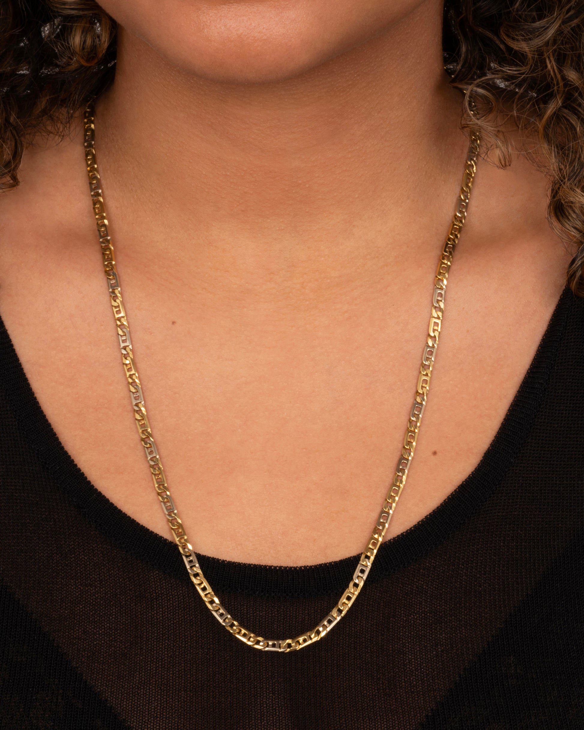 A white and yellow gold geometric flat chain necklace. Shown worn around a neck.