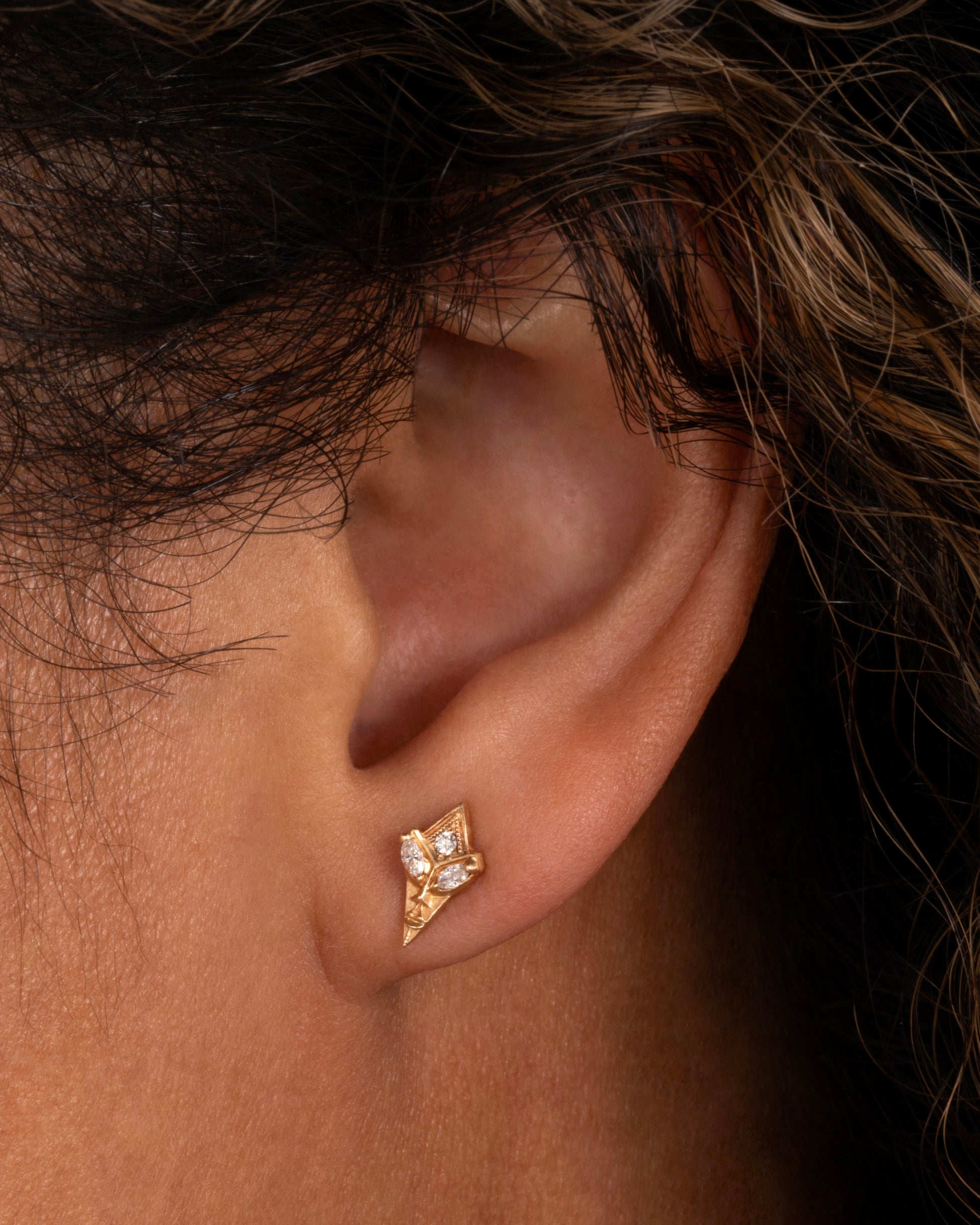 A pair of yellow gold alien earrings with diamond eyes. Shown worn in an ear.