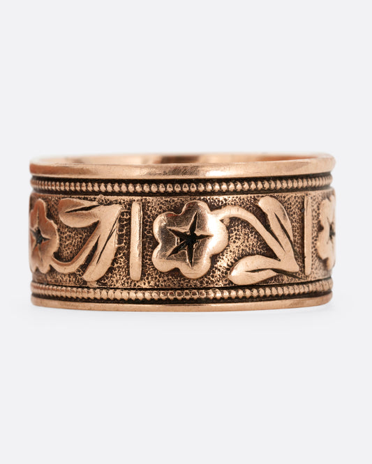 A rose gold cigar band with flowers along the middle. Shown from the front.