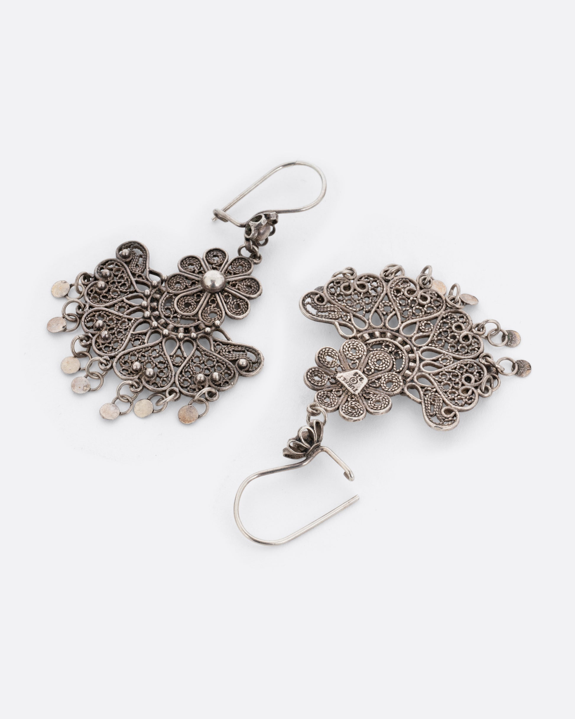 A pair of silver chandelier earrings with daisies on the ear hooks and filigree work below. There are seven tiny dangling disc charms hanging at the bottom of each earring. One earring is shown from the front, the other is shown from the back with an open ear hook.