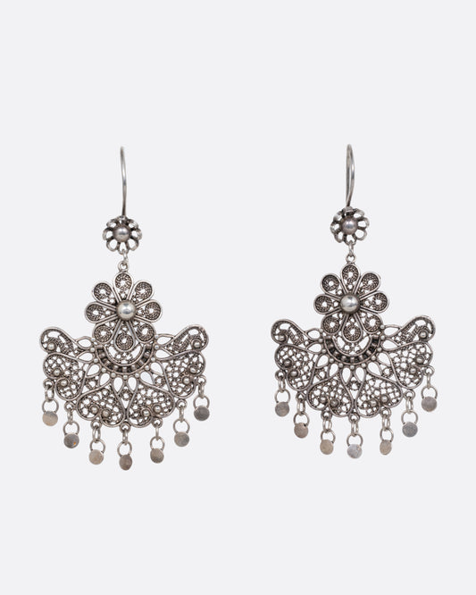 A pair of silver chandelier earrings with daisies on the ear hooks and filigree work below. There are seven tiny dangling disc charms hanging at the bottom of each earring. Shown from the front.