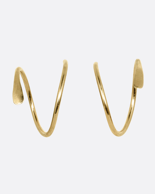 A pair of yellow gold earrings in a loop shape with one hammered flat end. Shown on their sides from the front.