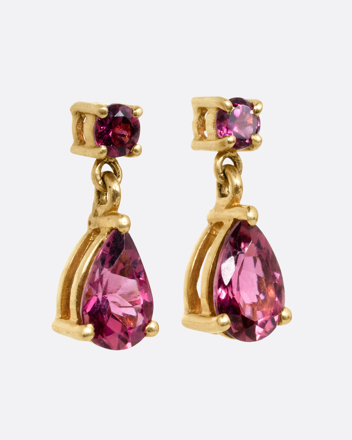 Yellow gold earrings with round prong set pink tourmalines at the top and teardrop shaped pink tourmalines at the bottom. Shown from the side.