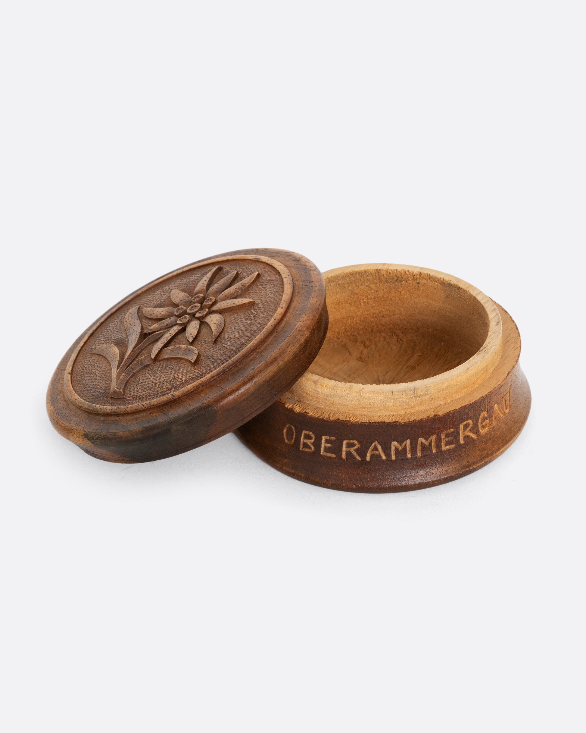A circular hand carved wooden box with 'Oberammergau', a town in Germany, around its base and a flower on its top. Shown open from the side.