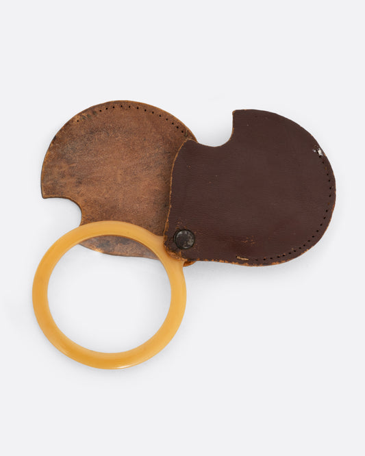A plastic circular magnifying lens with a yellow edge. The lens slides out from a circular leather case. Shown open from the front.
