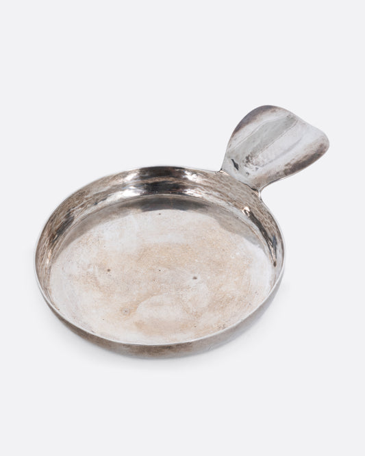 A round silver ashtray with a ledge for placing a cigarette. Shown from the top at an angle.