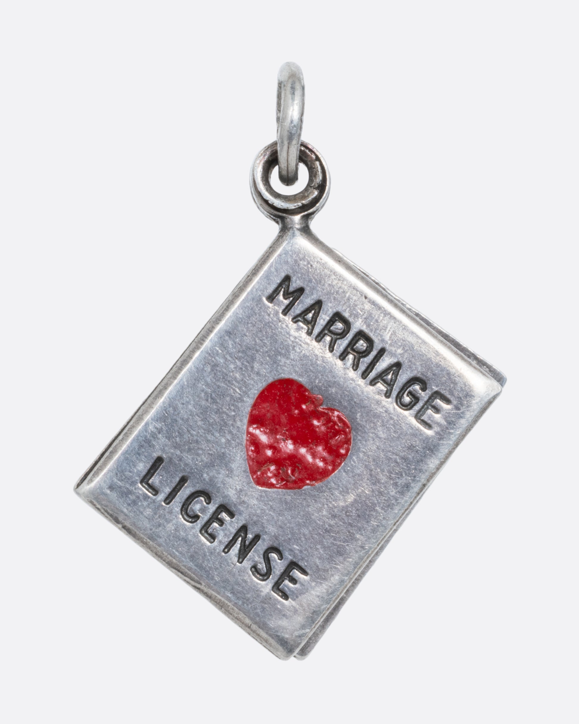 A silver marriage license charm with a red heart on the front. 