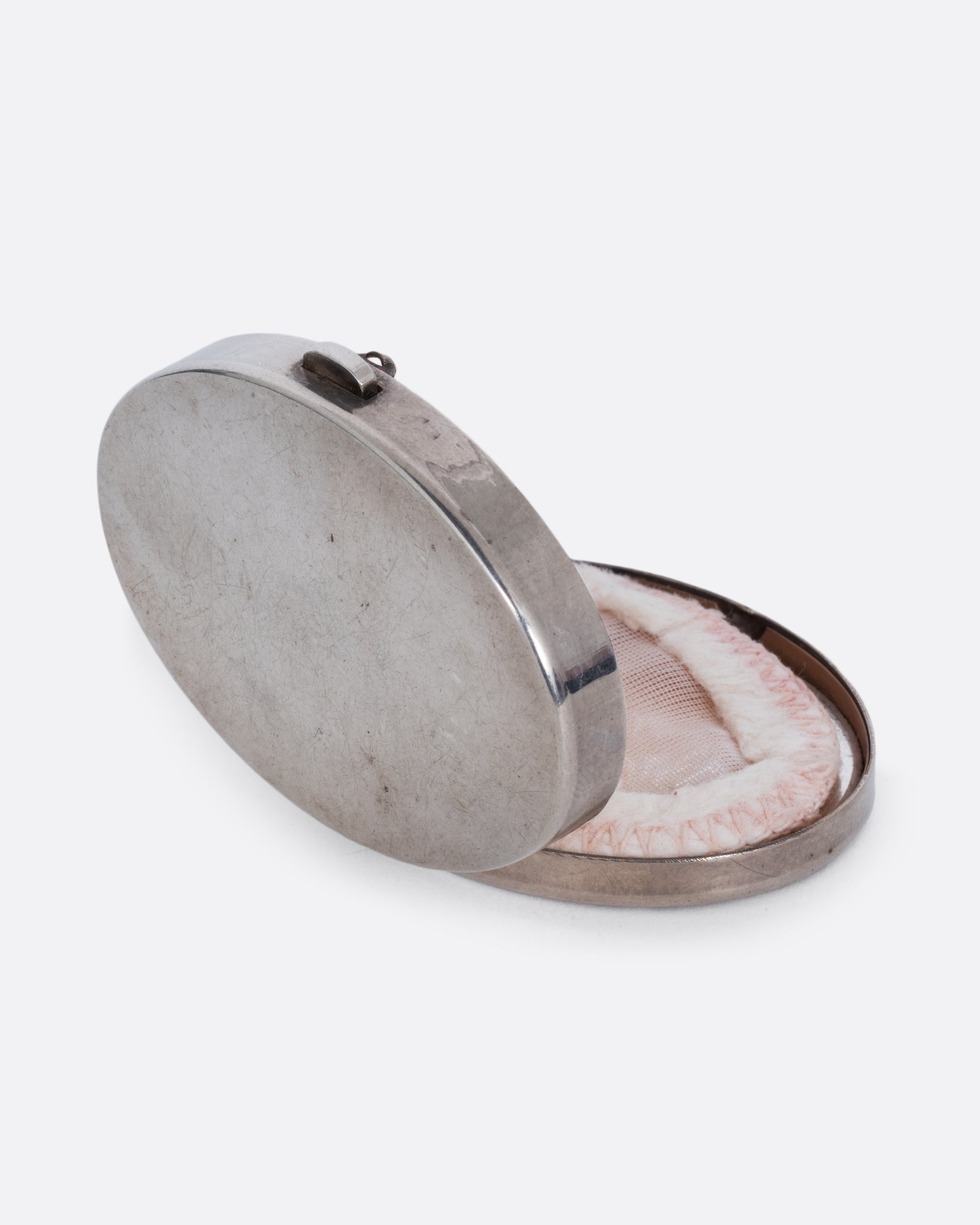 A silver mirror compact shown open at an angle from the back with a powder puff inside.