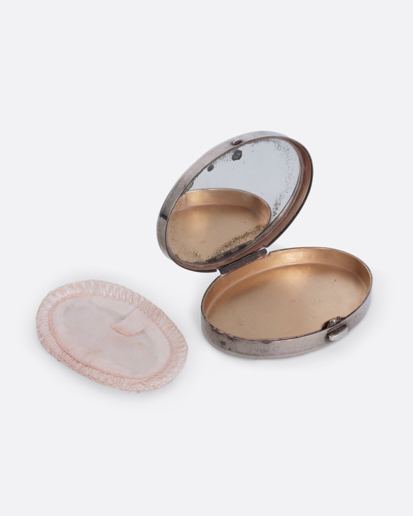 A silver mirror compact shown open at an angle from the front with a powder puff sitting at its side.
