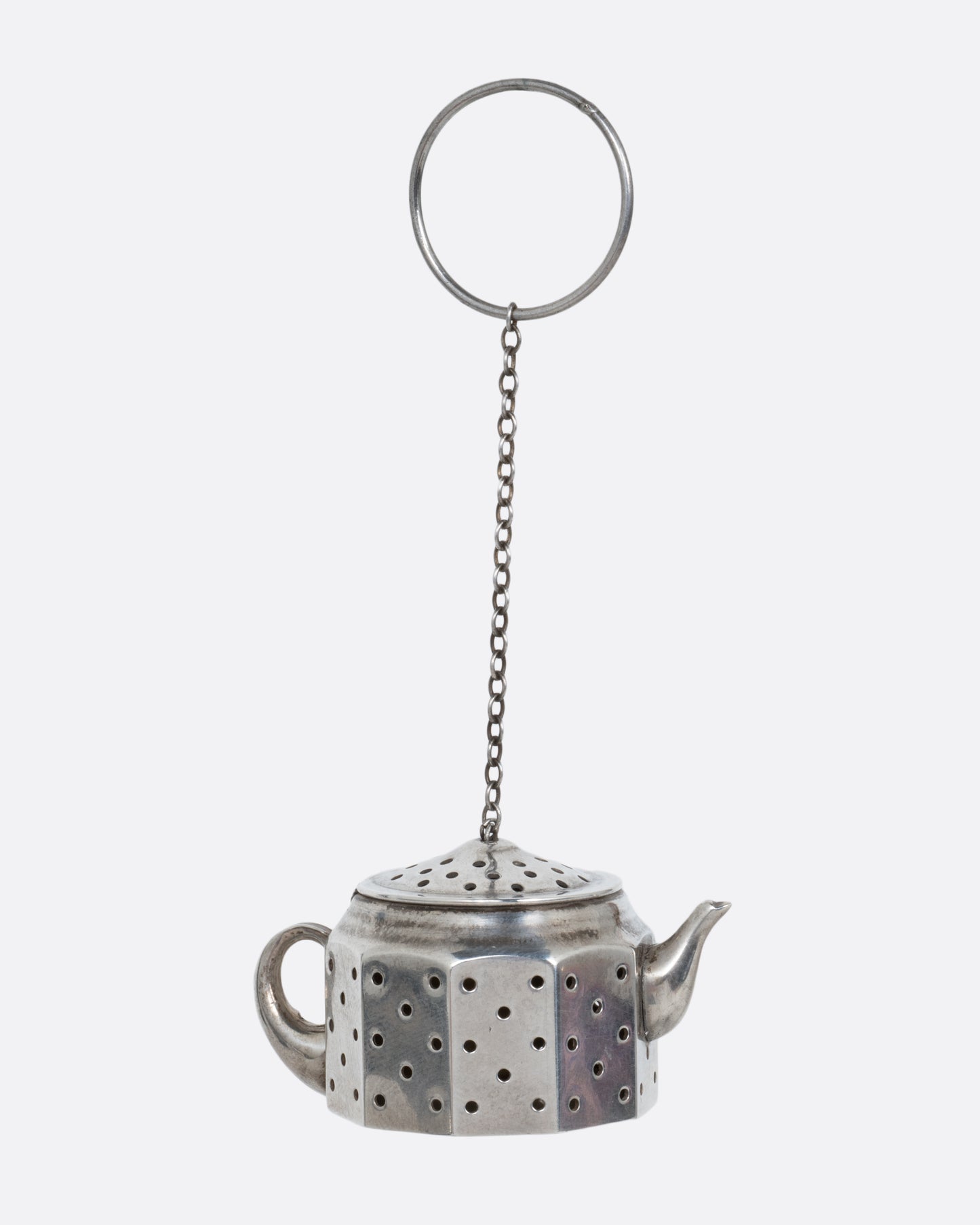 A silver teapot shaped tea infuser with a chain and hoop attached to the lid. Shown from the side.