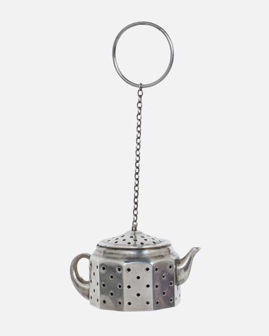 A silver teapot shaped tea infuser with a chain and hoop attached to the lid. Shown from the side.