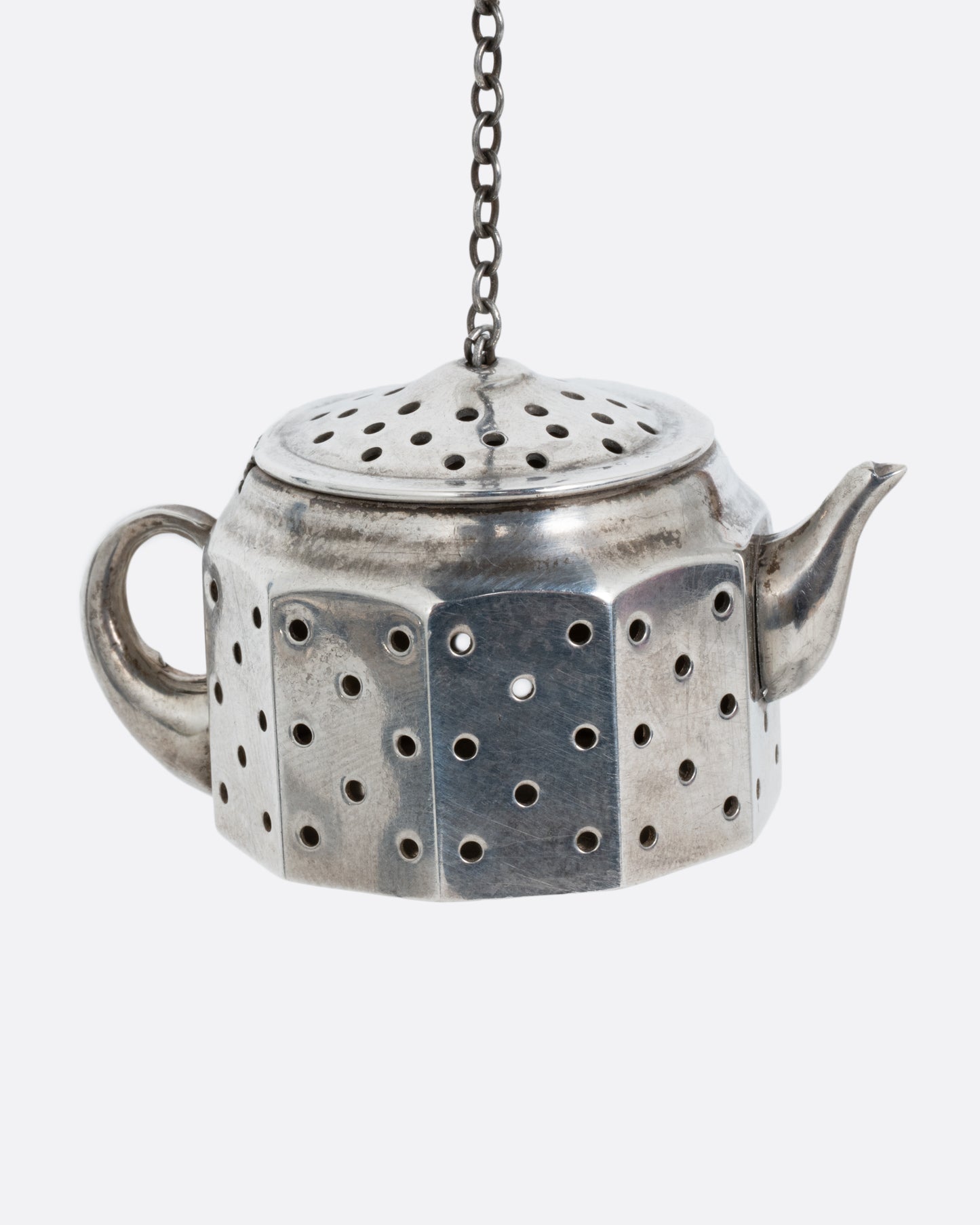 A silver teapot shaped tea infuser with a chain attached to the lid. Shown from the side.