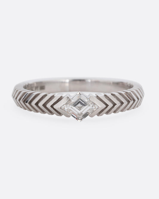 A platinum ring with a 'pleated' motif and lozenge shaped diamond at the center. Shown from the front.