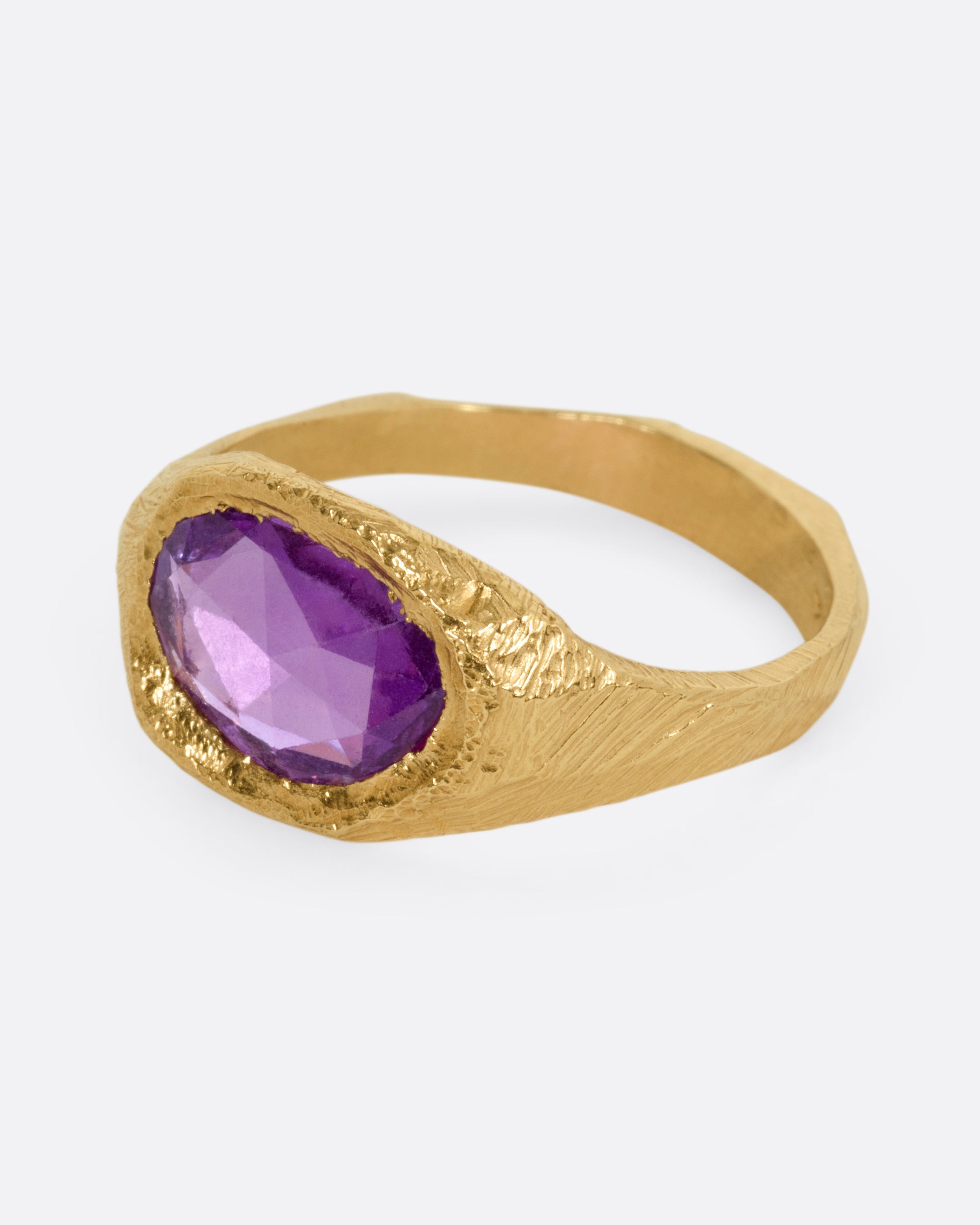 A yellow gold ring with a purple sapphire, shown from the side.