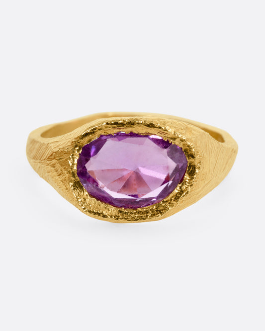 A yellow gold ring with a purple sapphire, shown from the front.