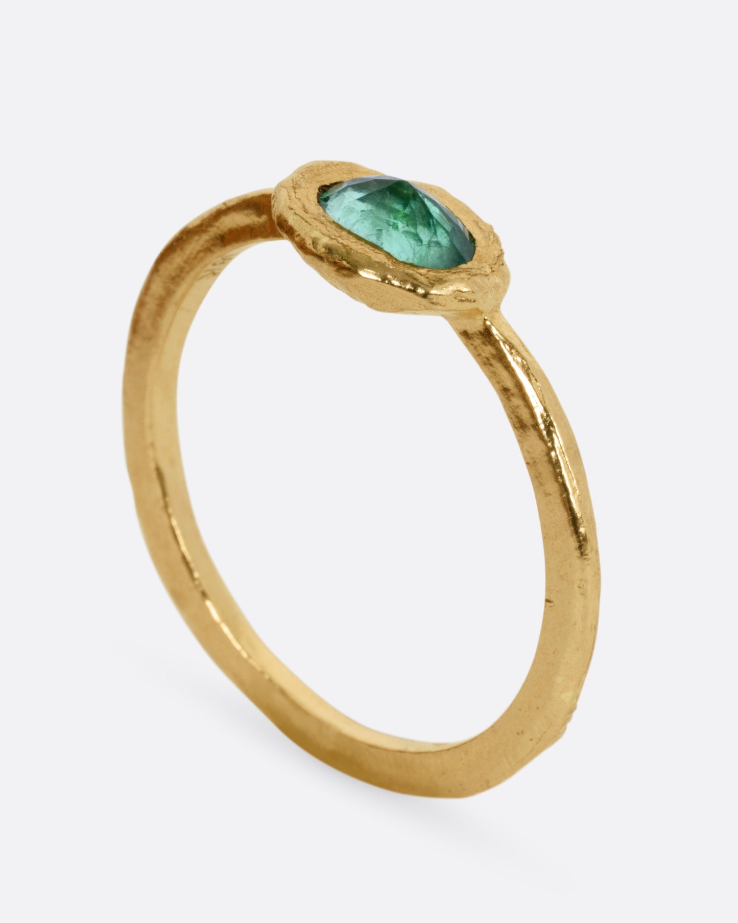 A yellow gold ring with an oval emerald, shown from the side standing up.