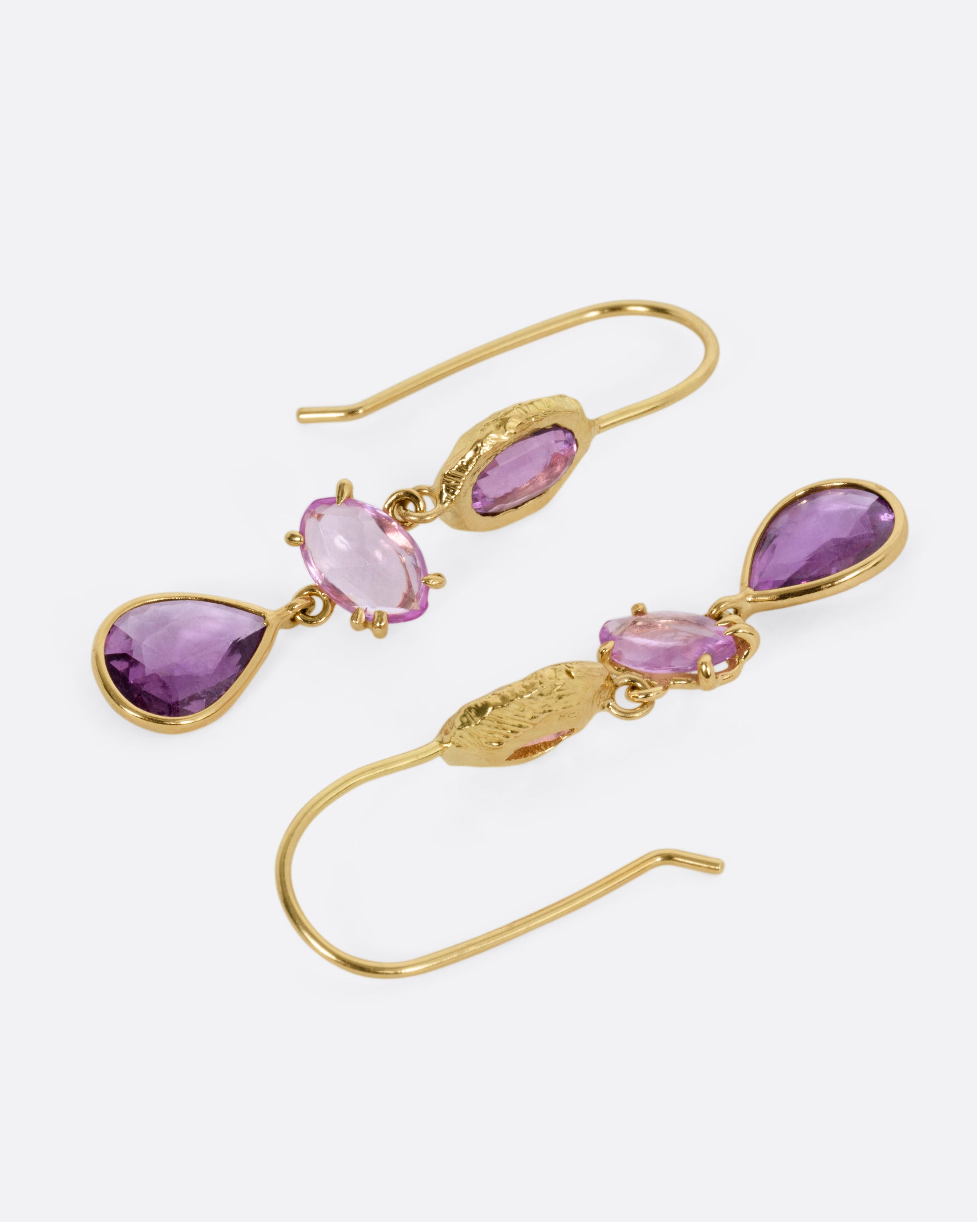 A pair of yellow gold earrings, each with three pink sapphires, shown lying flat.