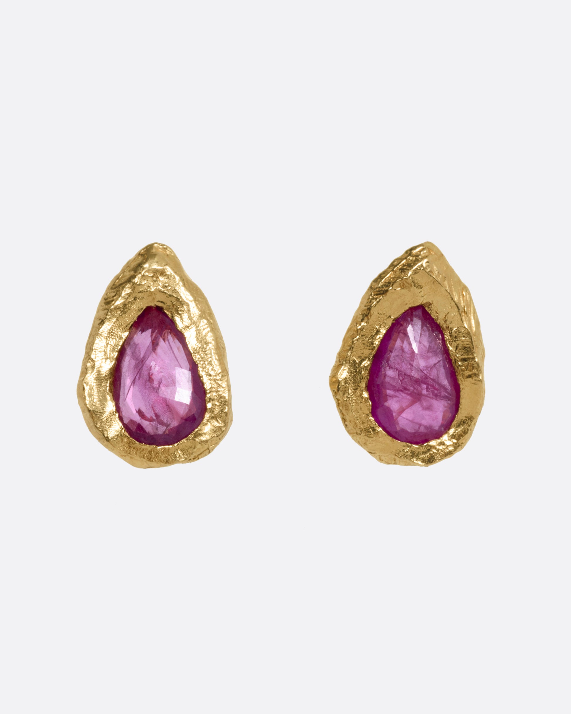 A pair of yellow gold stud earrings with teardrop shaped rubies, shown from the front.