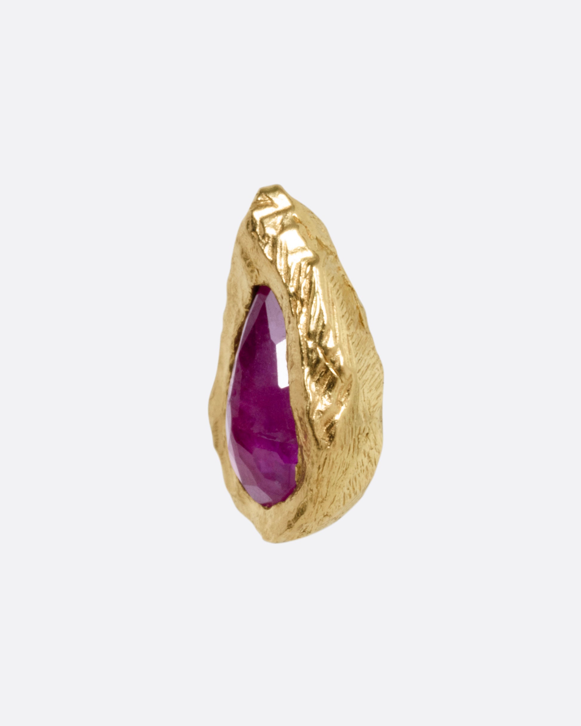A yellow gold stud earring with a teardrop shaped ruby, shown from the side.