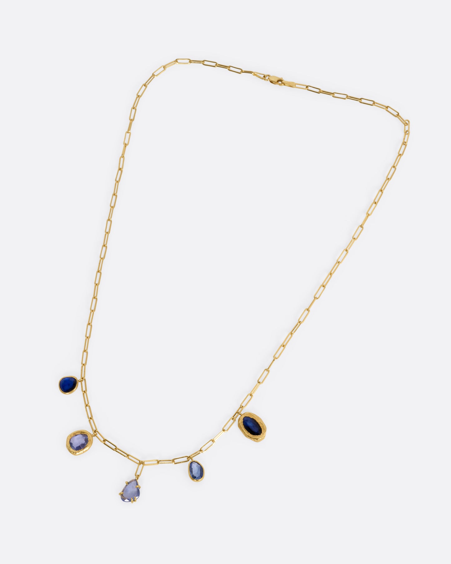 A yellow gold necklace with five blue sapphire charms, shown from the front.