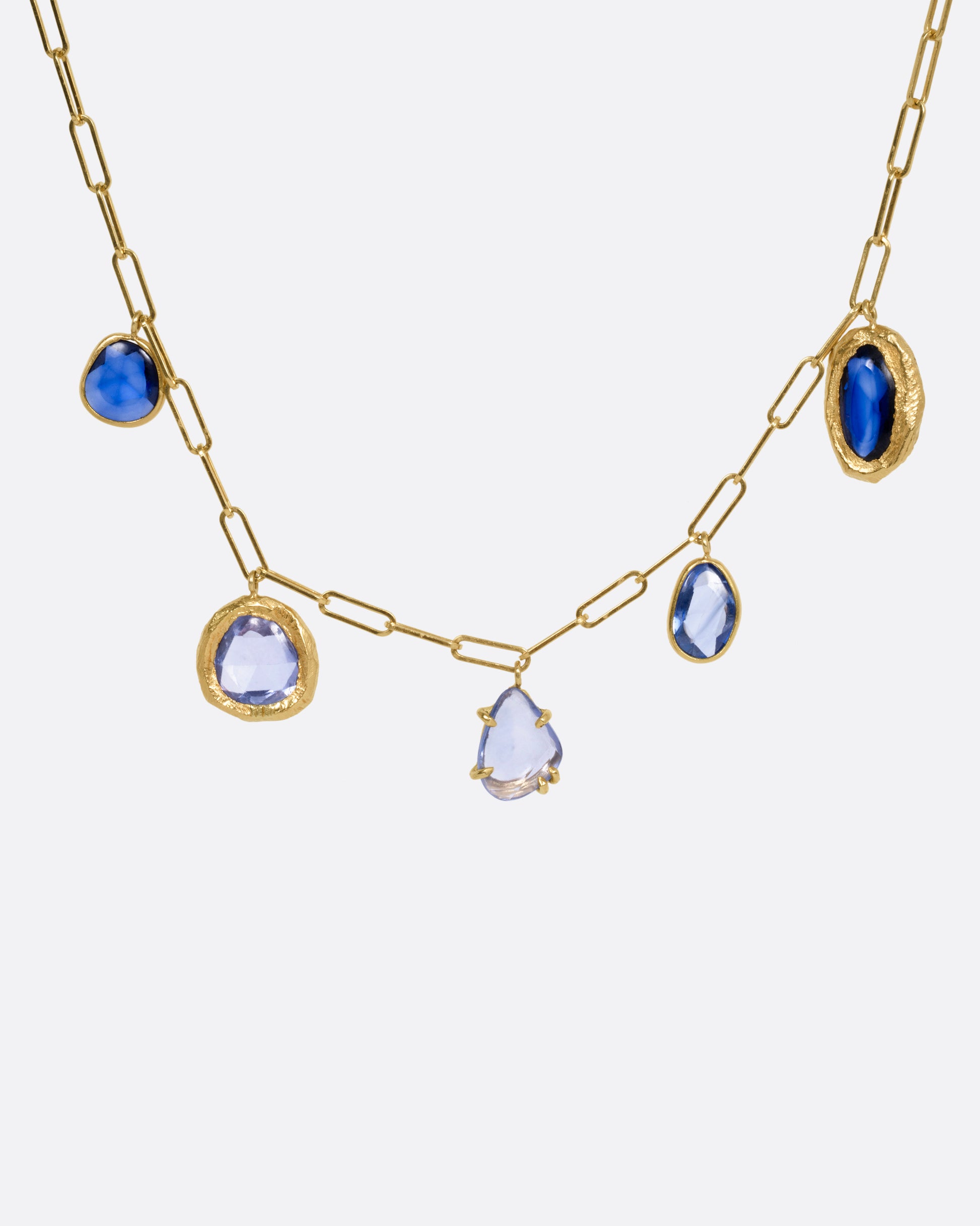 A yellow gold necklace with five blue sapphire charms, shown from the front.