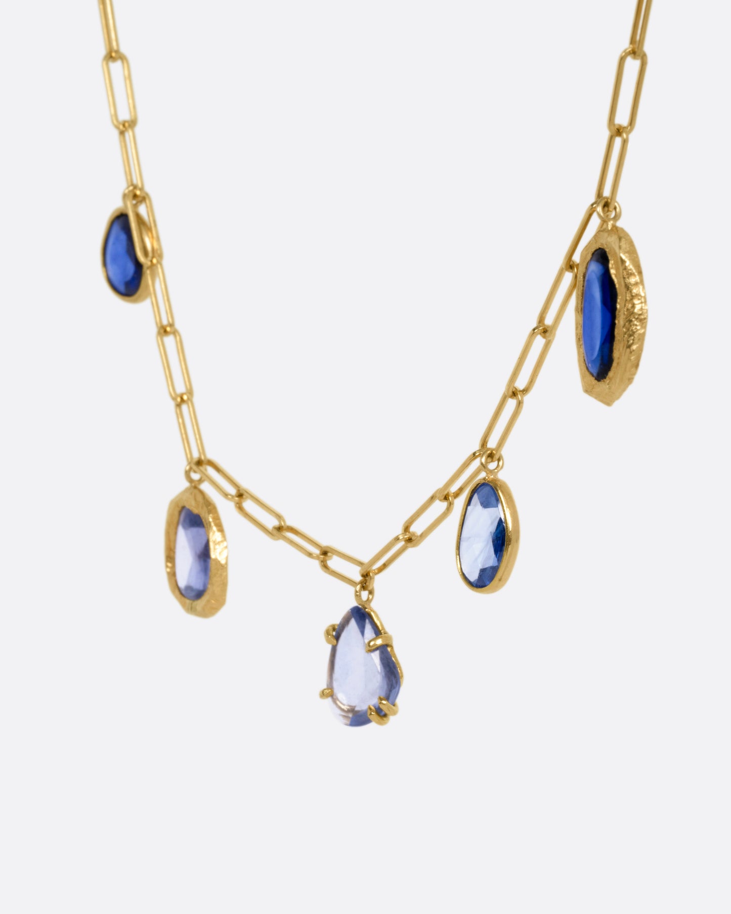 A yellow gold necklace with five blue sapphire charms, shown from the side.