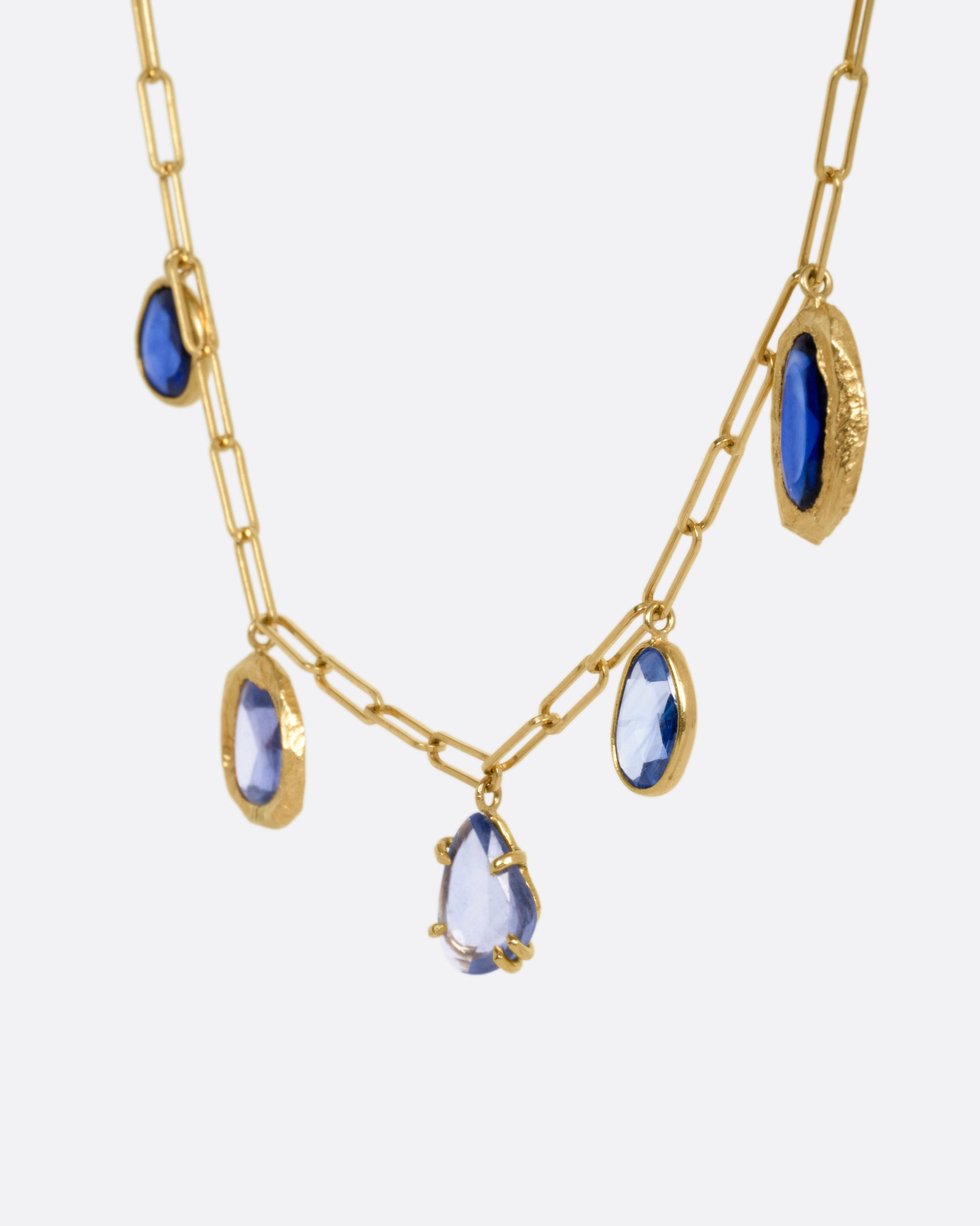A yellow gold necklace with five blue sapphire charms, shown from the side.