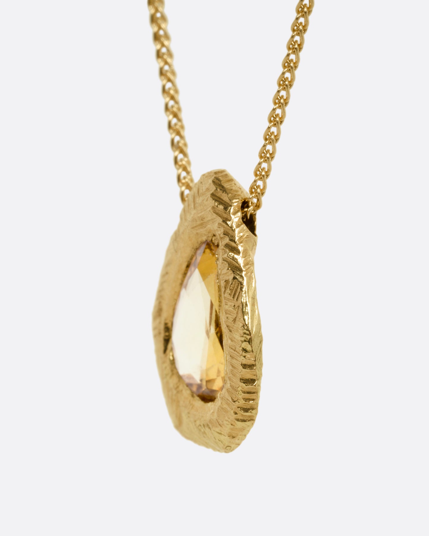 A yellow gold necklace with a yellow sapphire pendant, shown from the side.