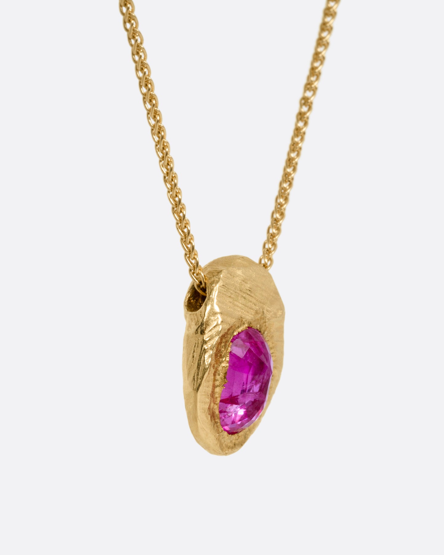 A yellow gold necklace with a ruby pendant shown from the side.
