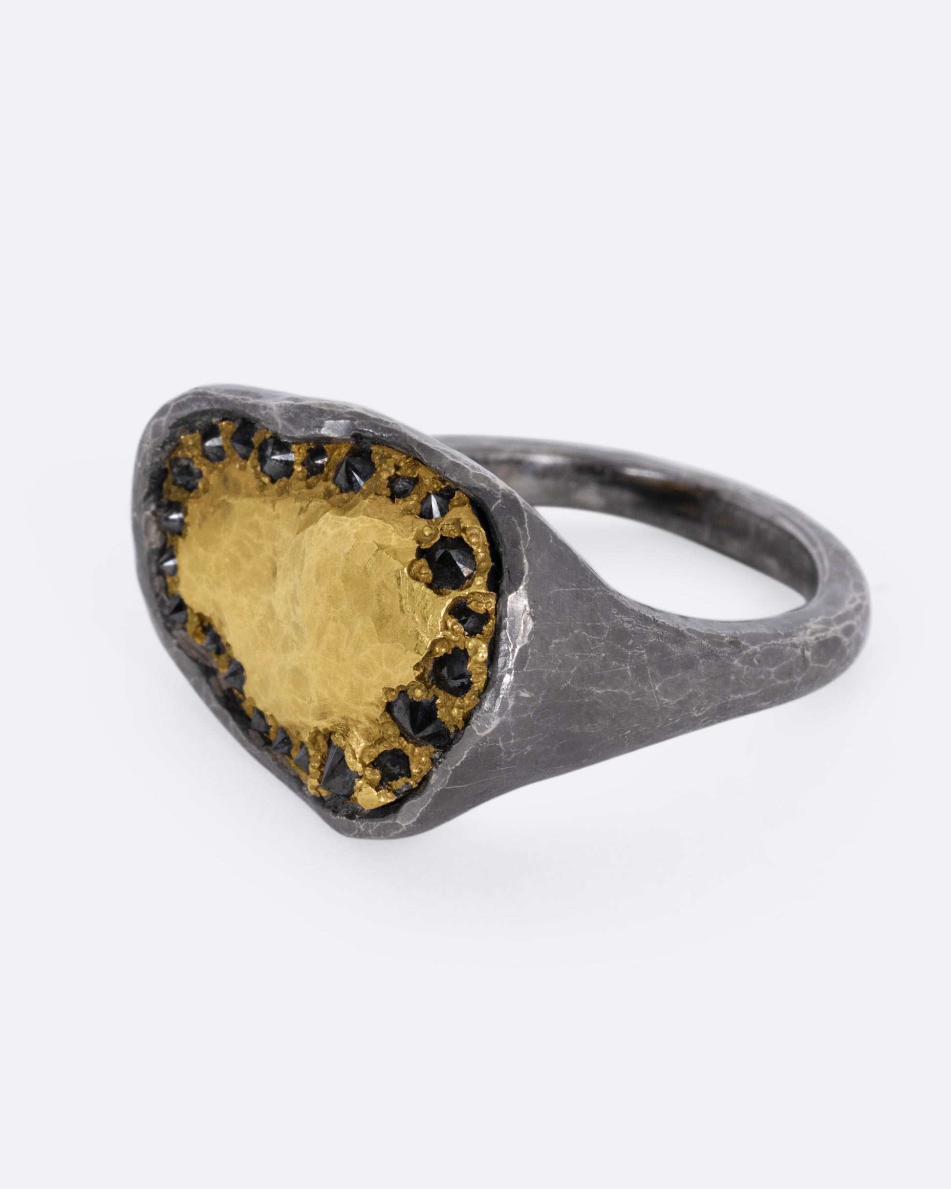 A white gold signet ring with a yellow gold face and a halo of reverse set black diamonds. Shown from the side.