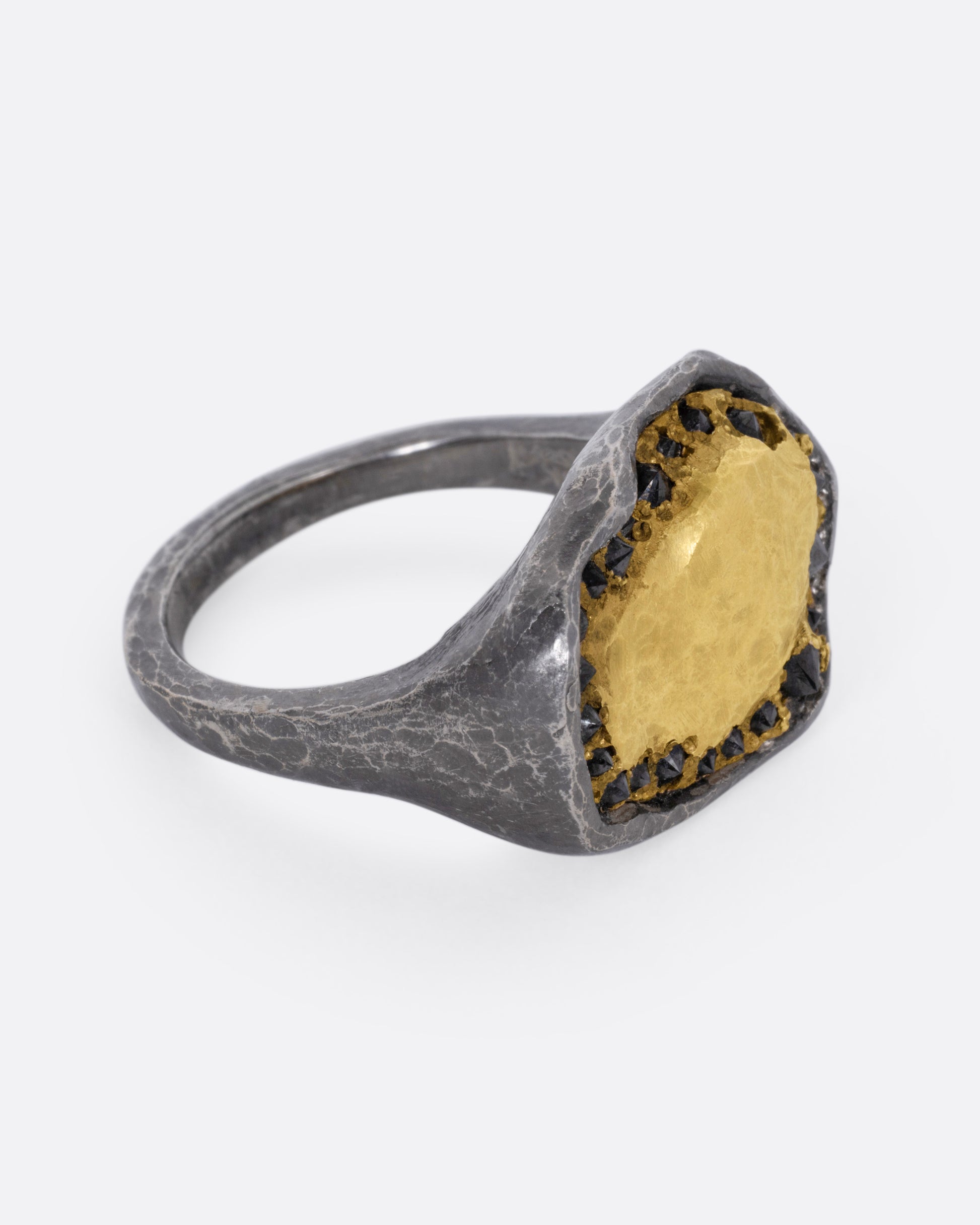 A white gold signet ring with a yellow gold face and a halo of reverse set black diamonds. Shown from the side.