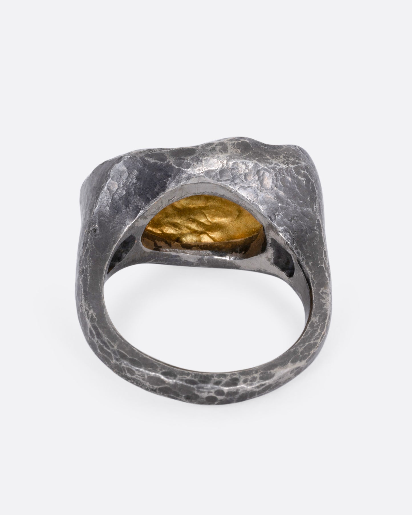 A white gold signet ring with a yellow gold face and a halo of reverse set black diamonds. Shown from the back.
