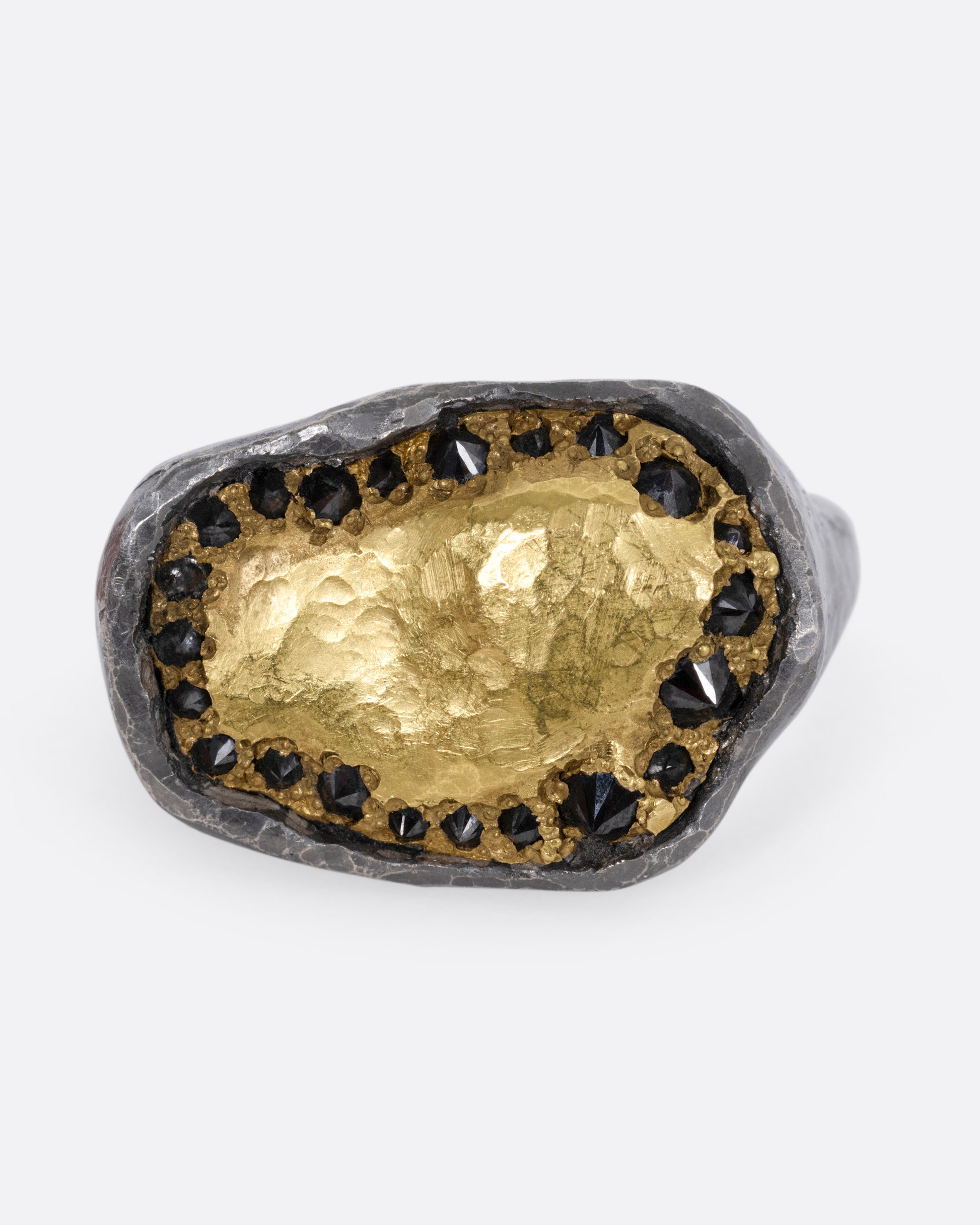A white gold signet ring with a yellow gold face and a halo of reverse set black diamonds. Shown from the front.