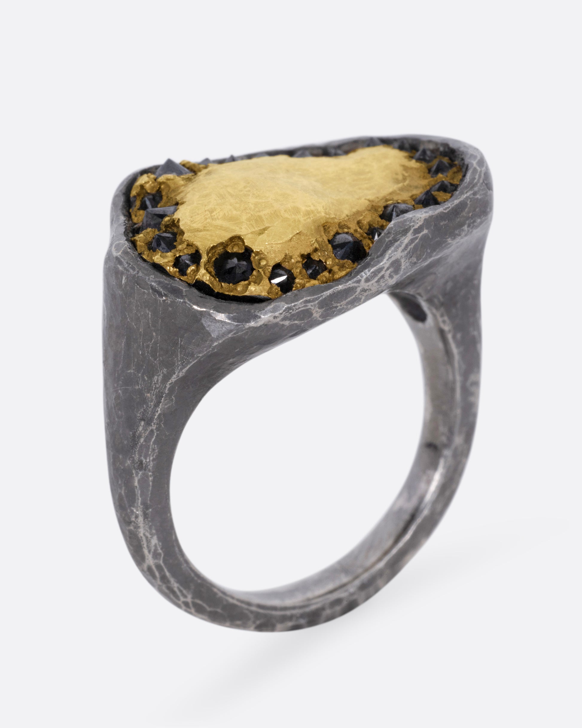 A white gold signet ring with a yellow gold face and a halo of reverse set black diamonds. Shown from the side standing up.