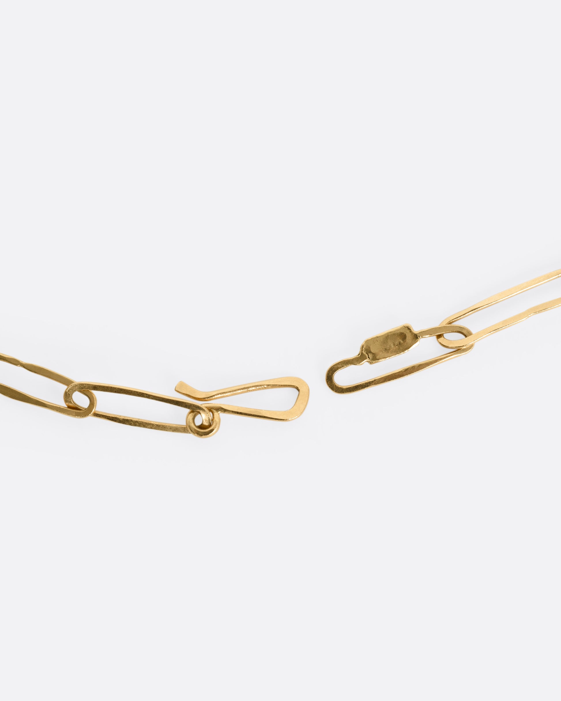 A close up of the clasp of a yellow gold paperclip chain.