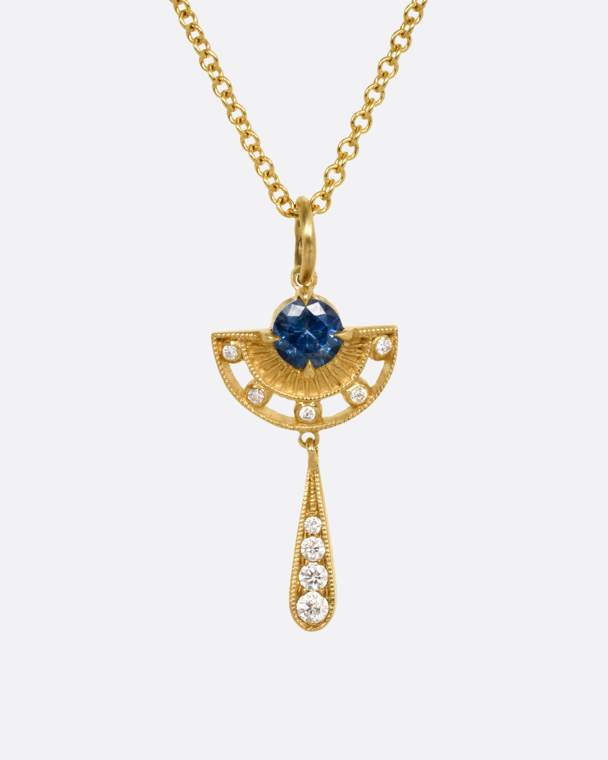 A yellow gold necklace with a sapphire and diamond pendant with open cutouts and a dangle drop. Shown from the front.