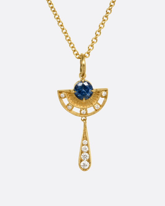 A yellow gold necklace with a sapphire and diamond pendant with open cutouts and a dangle drop. Shown from the front.