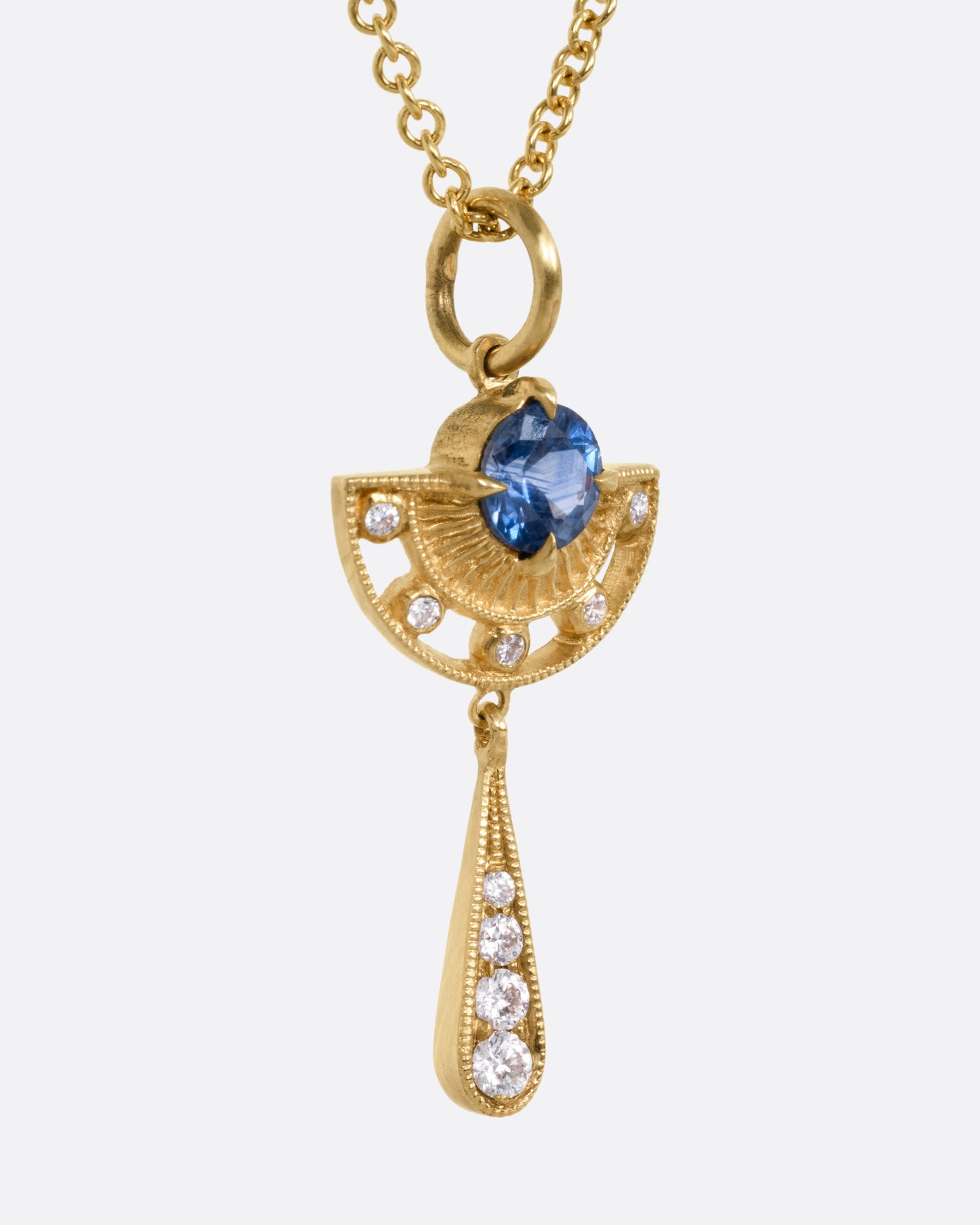 A yellow gold necklace with a sapphire and diamond pendant with open cutouts and a dangle drop. Shown from the side.