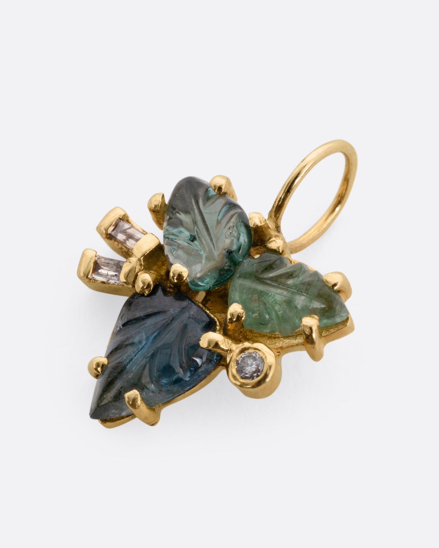 A yellow gold pendant with tourmalines and diamonds, in a botanical shape, shown lying flat from the side.