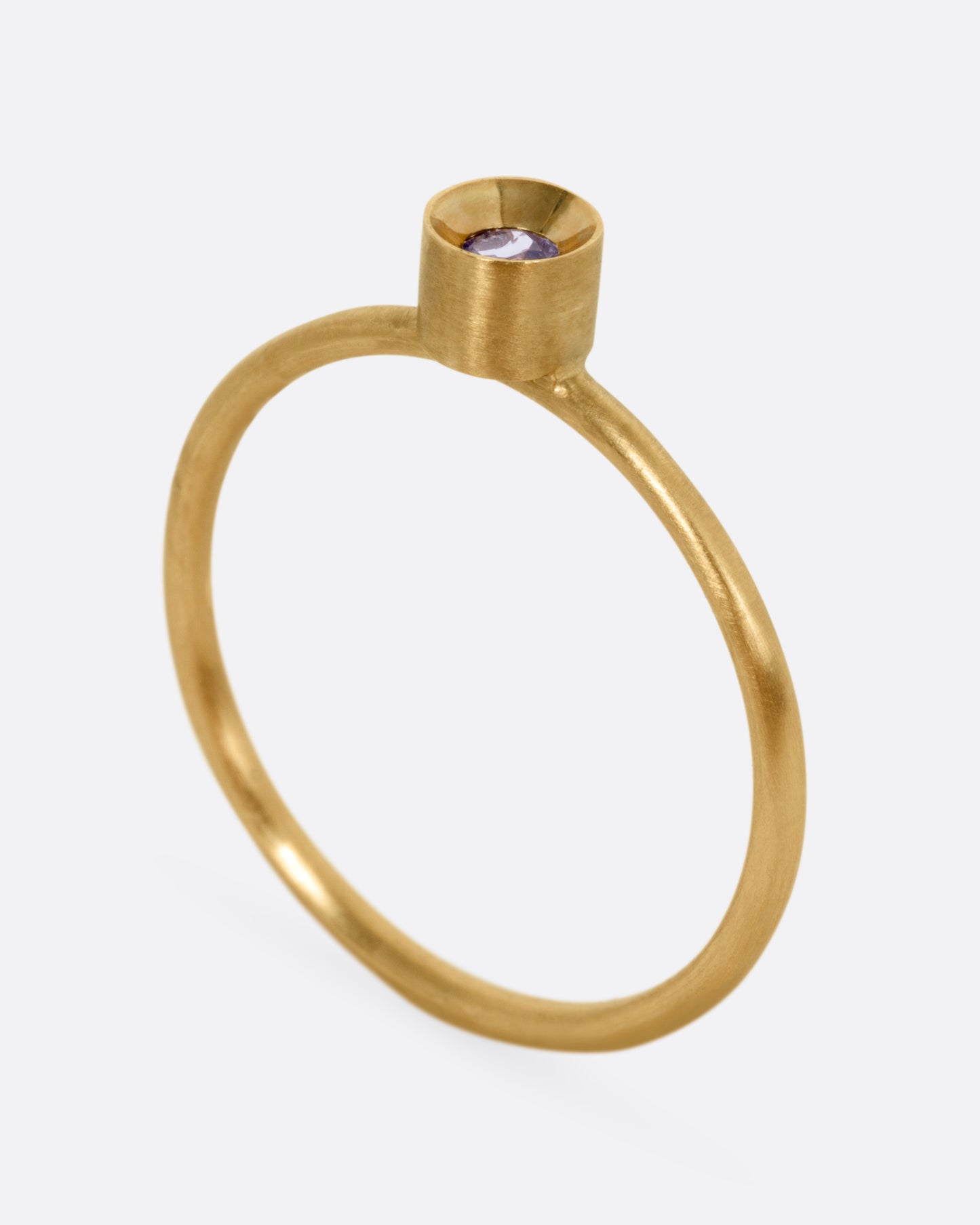 A yellow gold ring with a tanzanite in a raised bezel, shown from the side standing up.